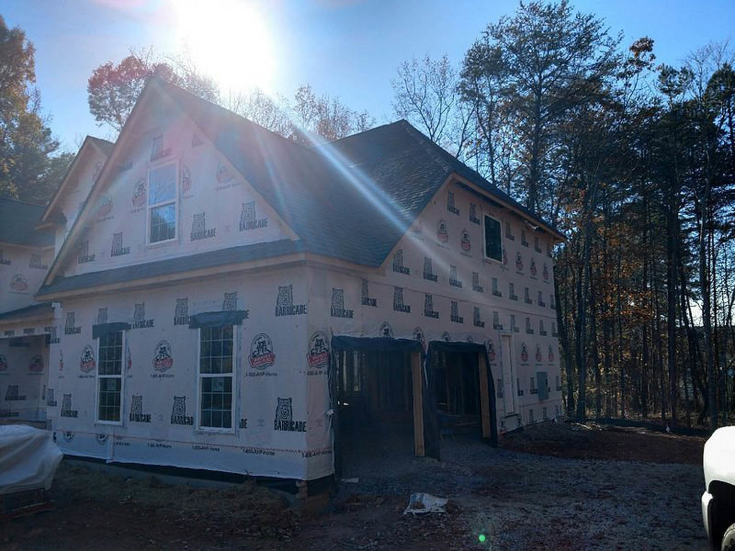 Framed custom home under construction with exposed wood beams, open window spaces, and surrounding trees in the background