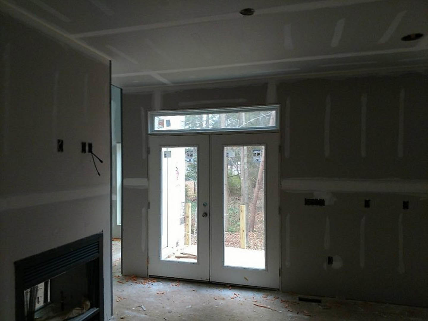 Living room with white plaster walls, glass-paneled double doors, large window, and modern fireplace on hardwood floor