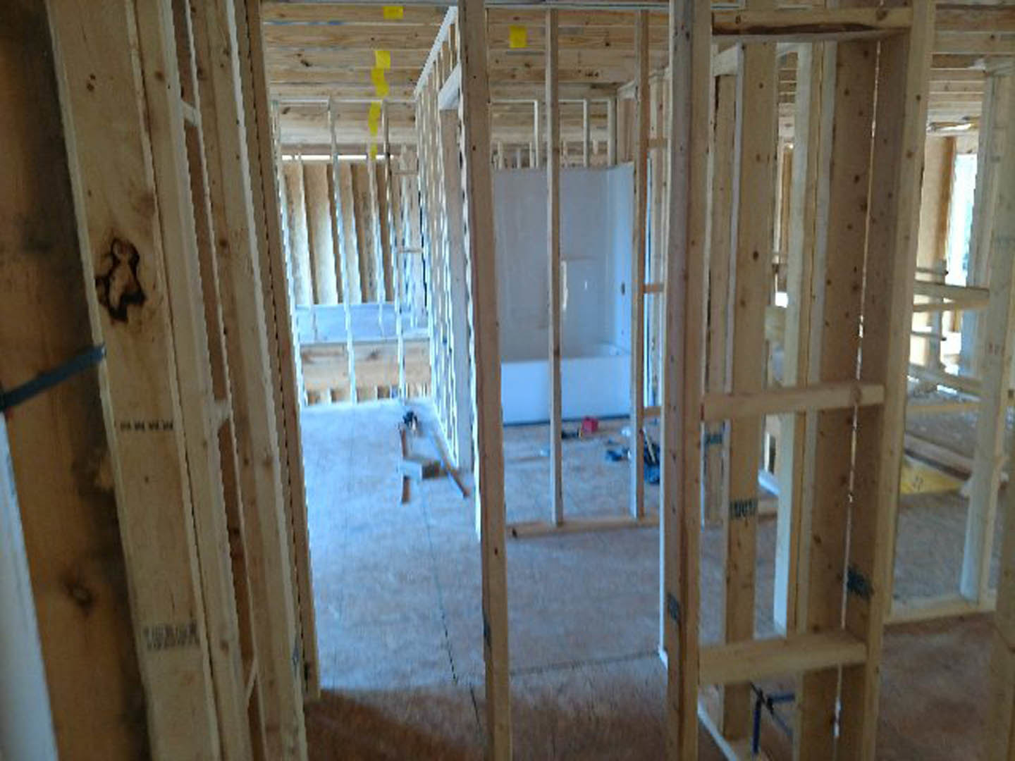 Bathroom with freestanding white bathtub, glass-enclosed shower, exposed wood framing, and unfinished floor during remodel.