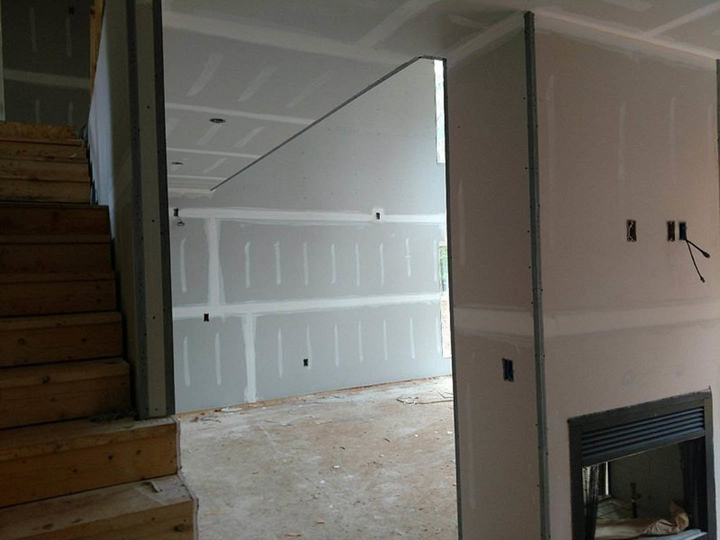 Open living space featuring a white plaster wall, wooden staircase with exposed steps, concrete flooring, and a modern fireplace.