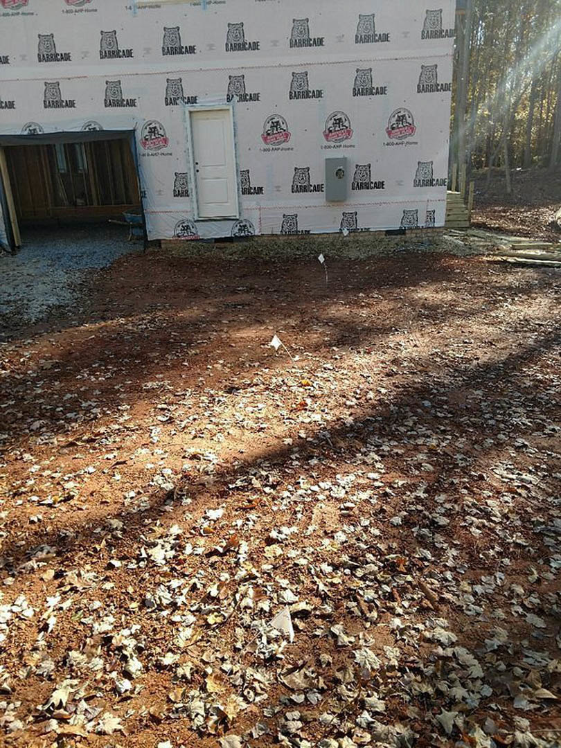White exterior wall with a white door featuring black knobs and a bear logo, brown leaves scattered across the ground, person riding a bike nearby