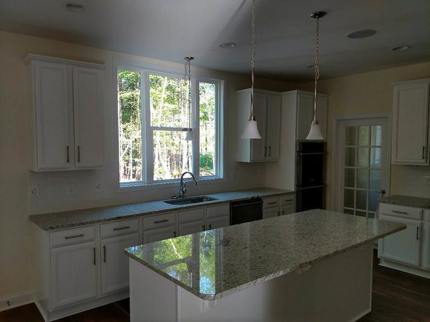 Spacious kitchen featuring a large central island with polished countertop reflecting trees from nearby window, dark cabinetry, stainless steel sink, and modern appliances.