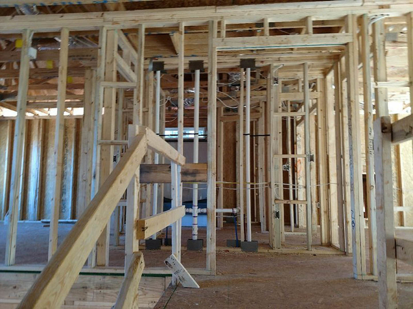 Exposed wooden framing and beams in a residential home under construction, with visible ladder, insulation, and unfinished plank surfaces.
