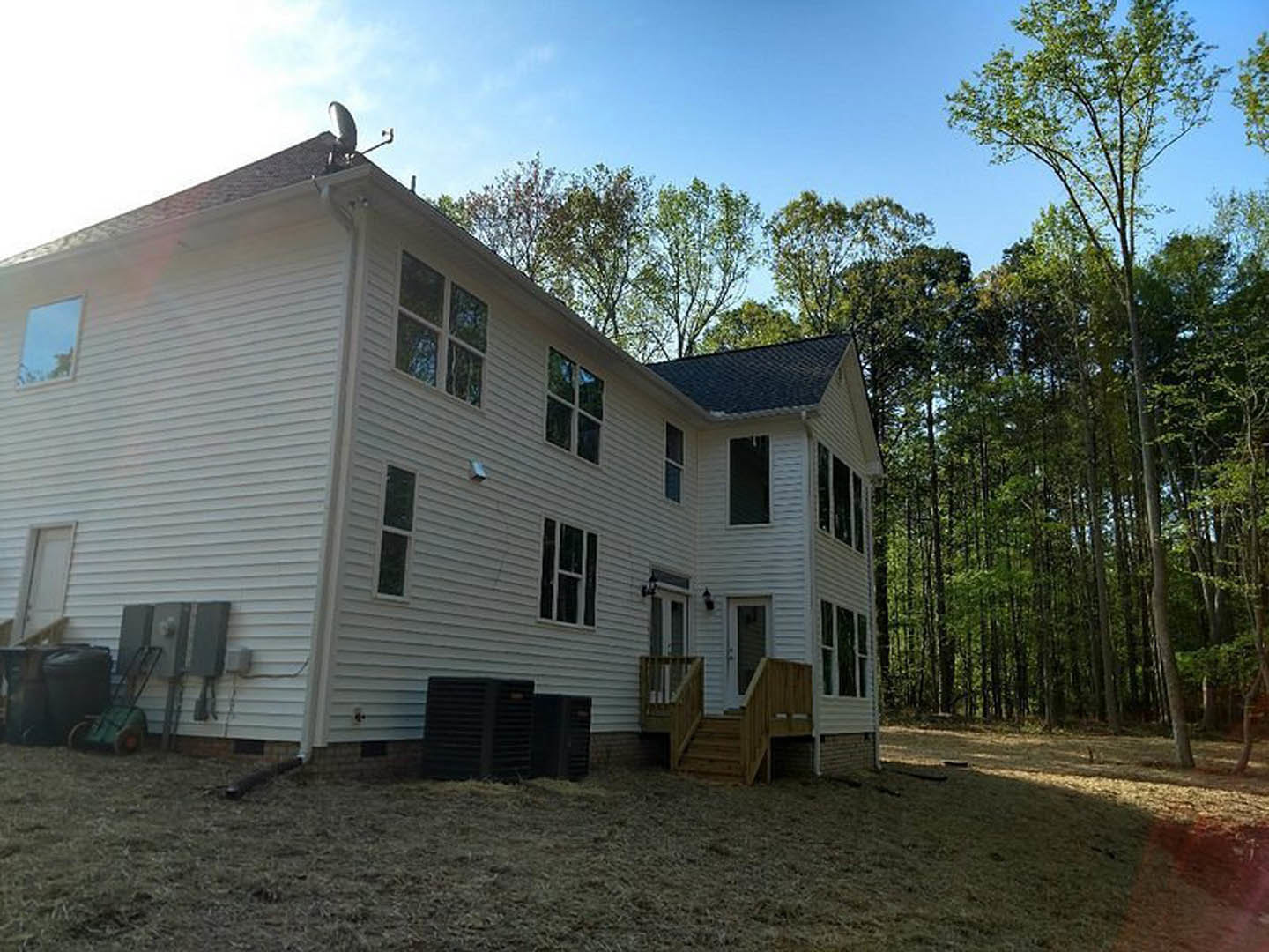 Two-story home with large covered porch, wooden exterior stairs, white trim windows, and mature trees in the background