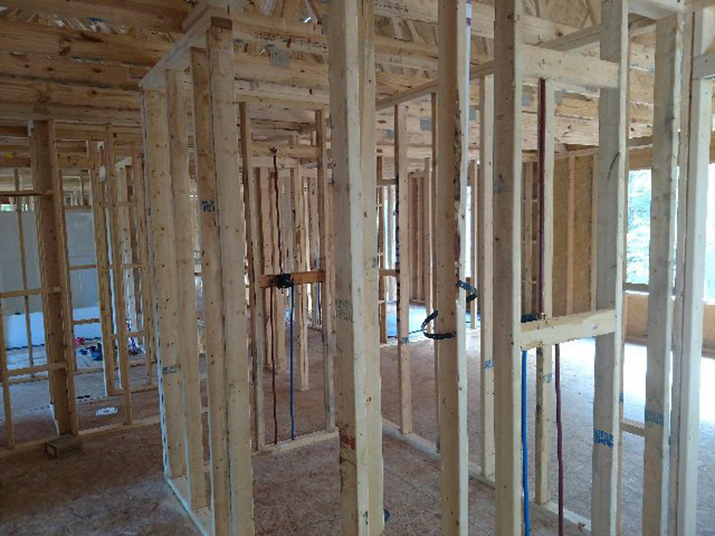 Exposed wood framing with vertical beams, blue plumbing pipe, building insulation, and unfinished ceiling and floor