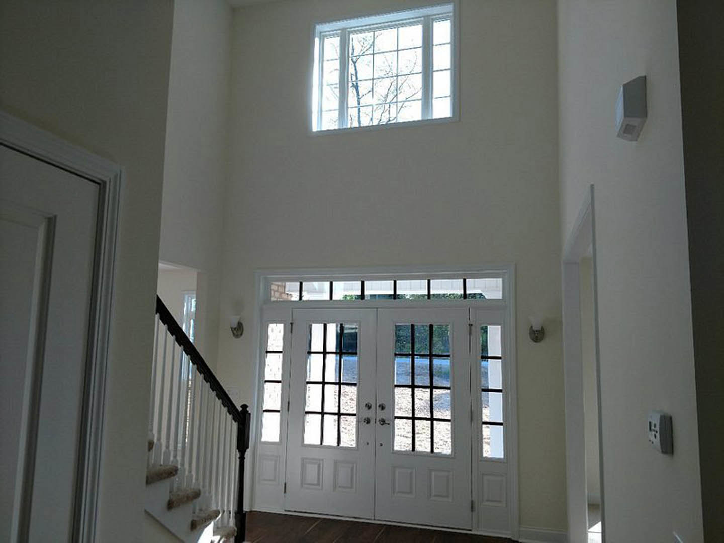 White double doors with glass panes, decorative molding, and adjacent window showing tree outside; staircase and light switch visible in foreground.