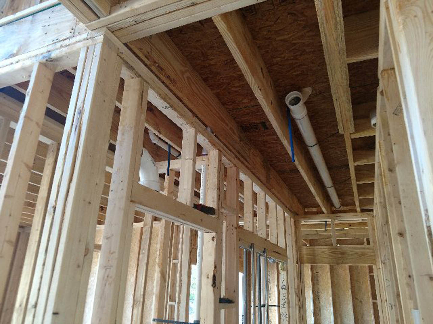 Exposed wood framing and beams inside a house under construction, white pipe with blue rope, unfinished ceiling with visible insulation and lumber