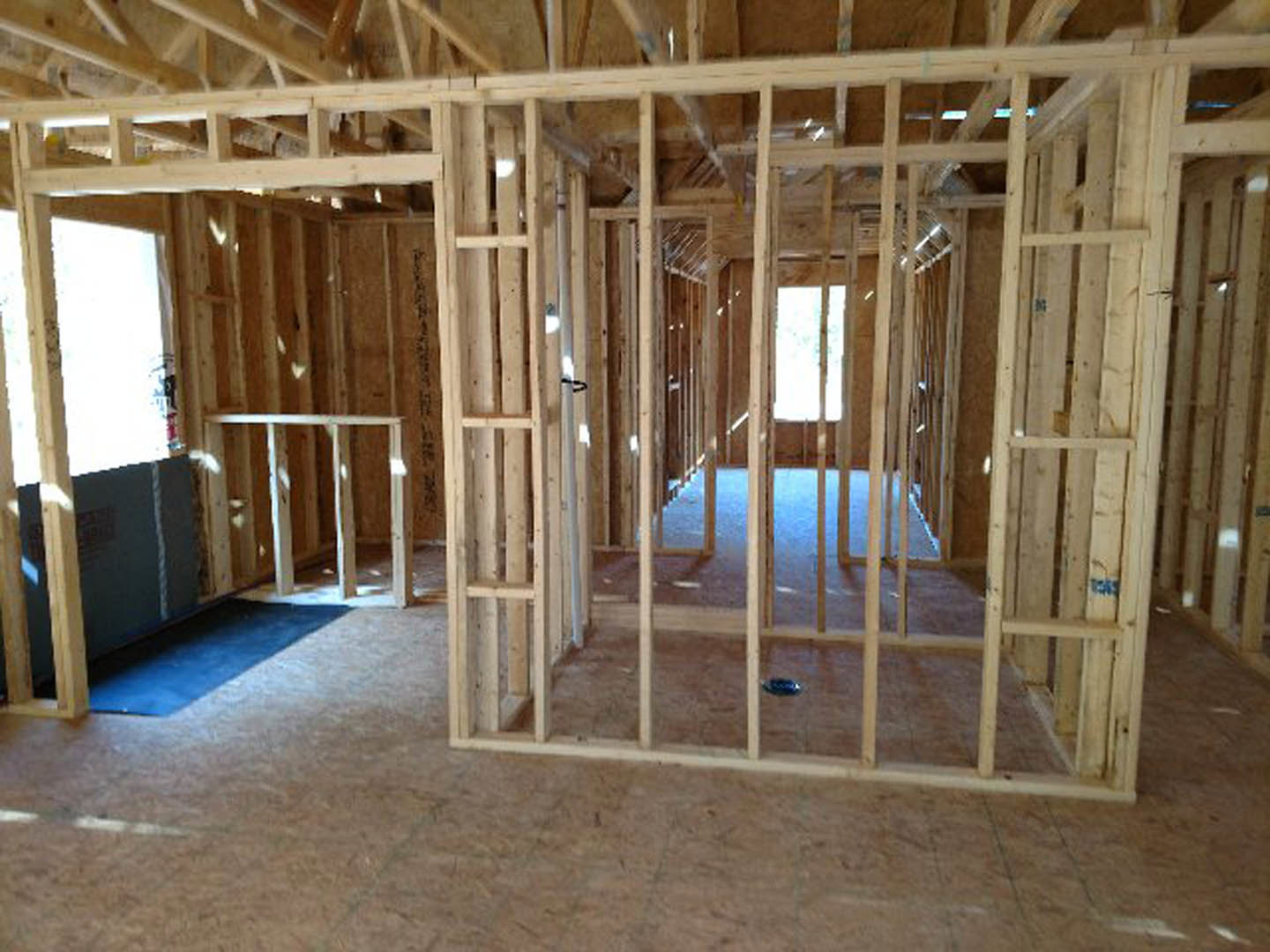 Wood-framed room under construction with exposed beams, unfinished walls, and a blue rug covering part of the subfloor