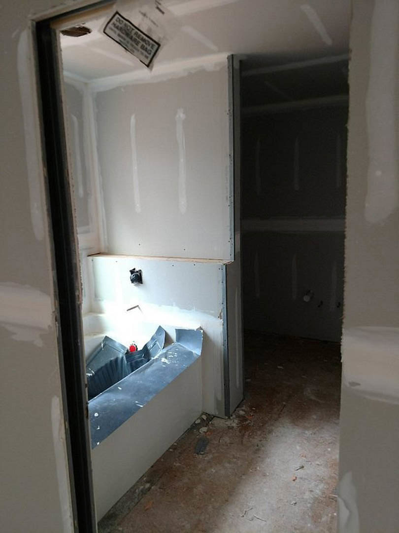 Bathroom under construction with exposed plaster walls, debris on the floor, a bathtub, light fixture, and a window covered by a plastic bag.