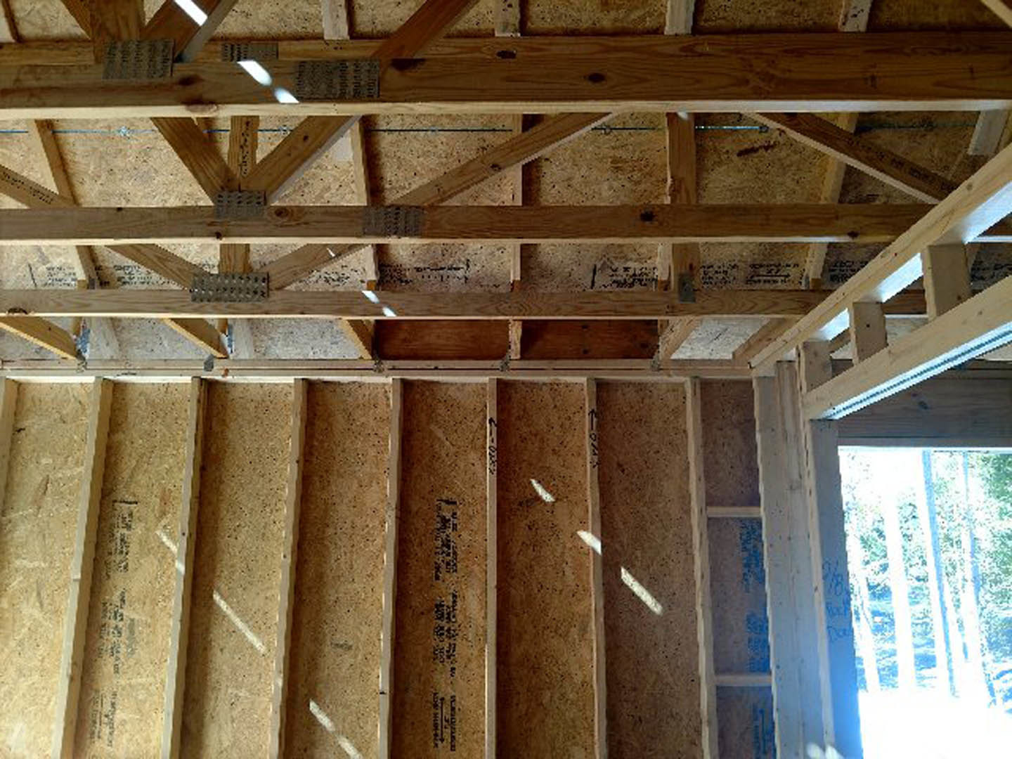 Exposed wooden beams and planks forming the interior frame of a house, blue building insulation visible along walls and ceiling