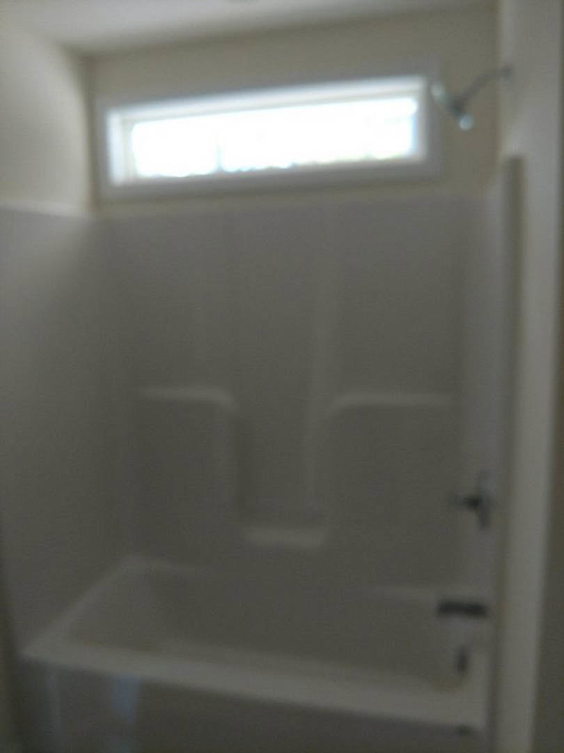 Freestanding white bathtub with chrome faucet beside large window, light gray tile floor, white walls, and minimal decor