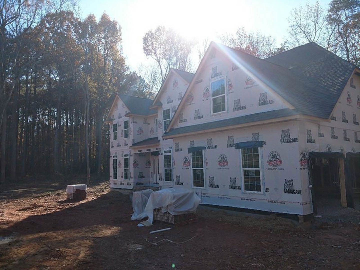 Modern white house exterior with large windows, covered patio area, and surrounding trees under a clear sky