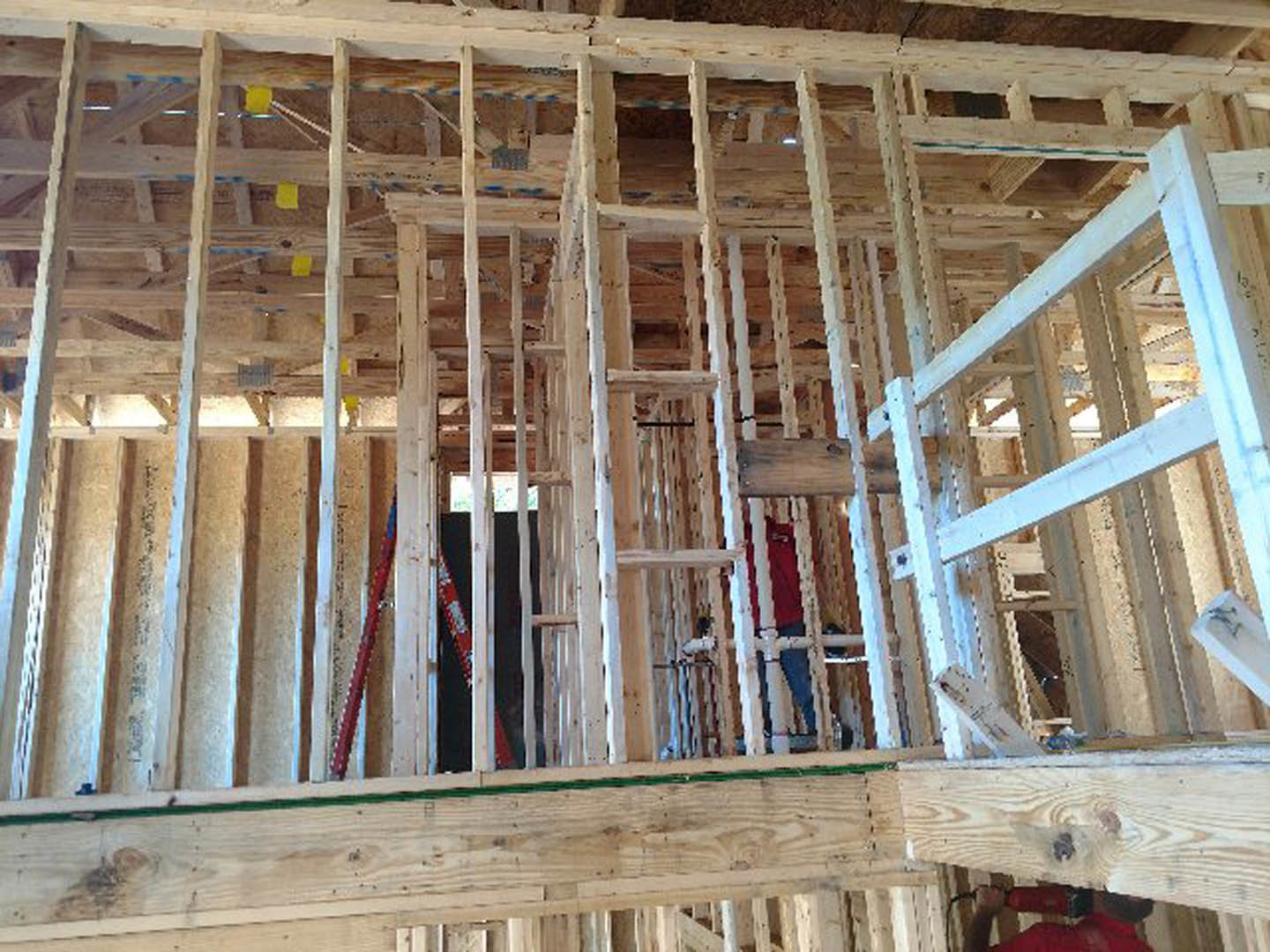 Exposed wood framing and beams inside a house under construction, with building insulation visible between studs