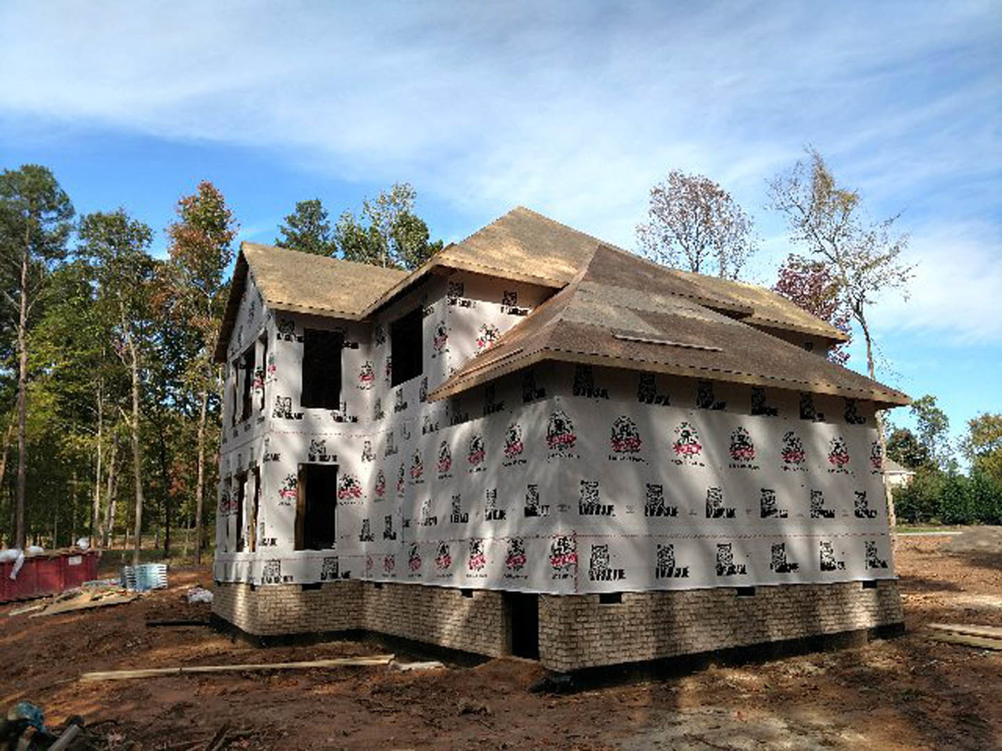Partially built brick house with exposed framing, surrounded by trees and cloudy sky in the background