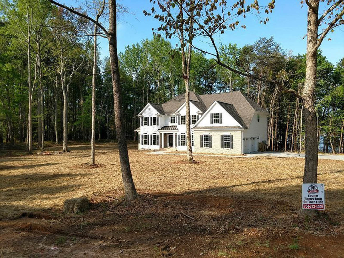 Modern two-story home with large windows, surrounded by mature trees and lush green lawn, blue sky overhead