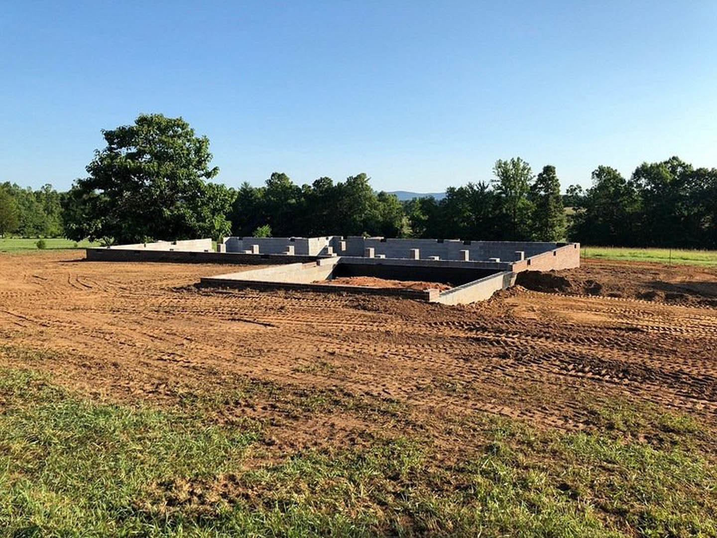 Concrete foundation set in a dirt field surrounded by trees, under a blue sky with scattered clouds