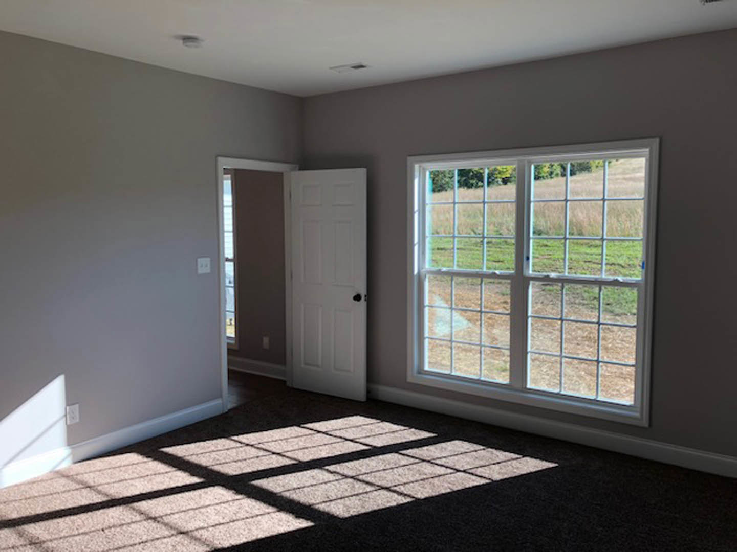White paneled door with black hardware, tile flooring, large window overlooking green grass and trees, cloudy sky visible outside