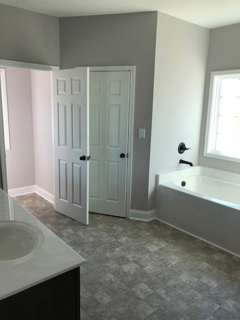 Bathroom with freestanding white bathtub, white sink, grey tile floor with white square tiles, white door, and window.