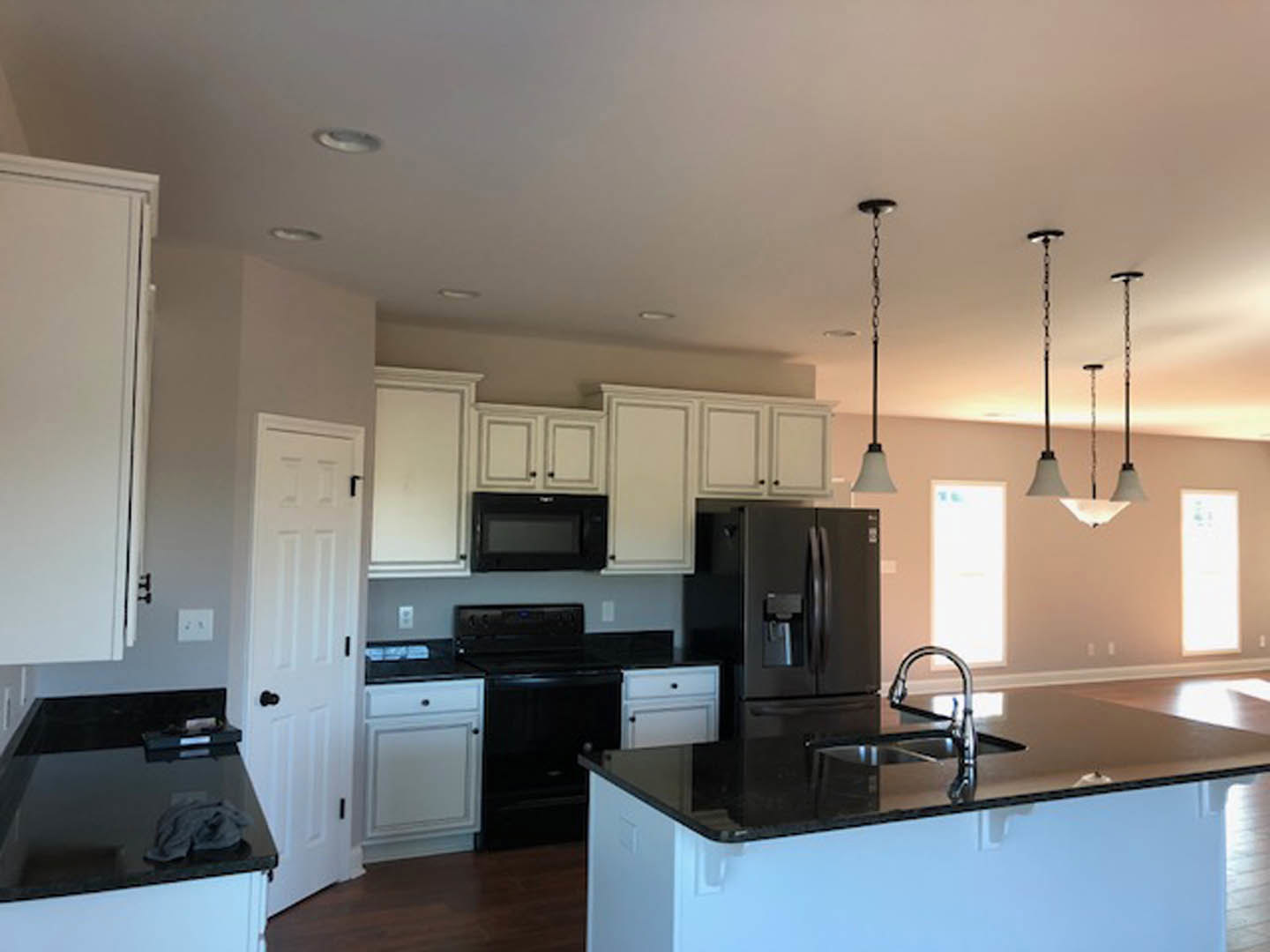 White shaker cabinets and black refrigerator in a modern kitchen with black countertops, stainless steel microwave, undermount sink, and pendant lighting