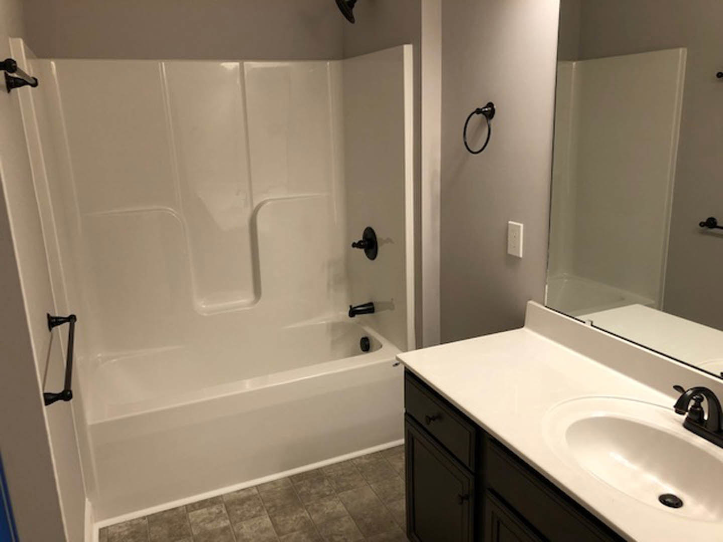 White tile bathroom featuring a glass-enclosed shower, white sink with round chrome faucet, black towel hook and holder mounted on the wall, and a white bathtub with black handles.