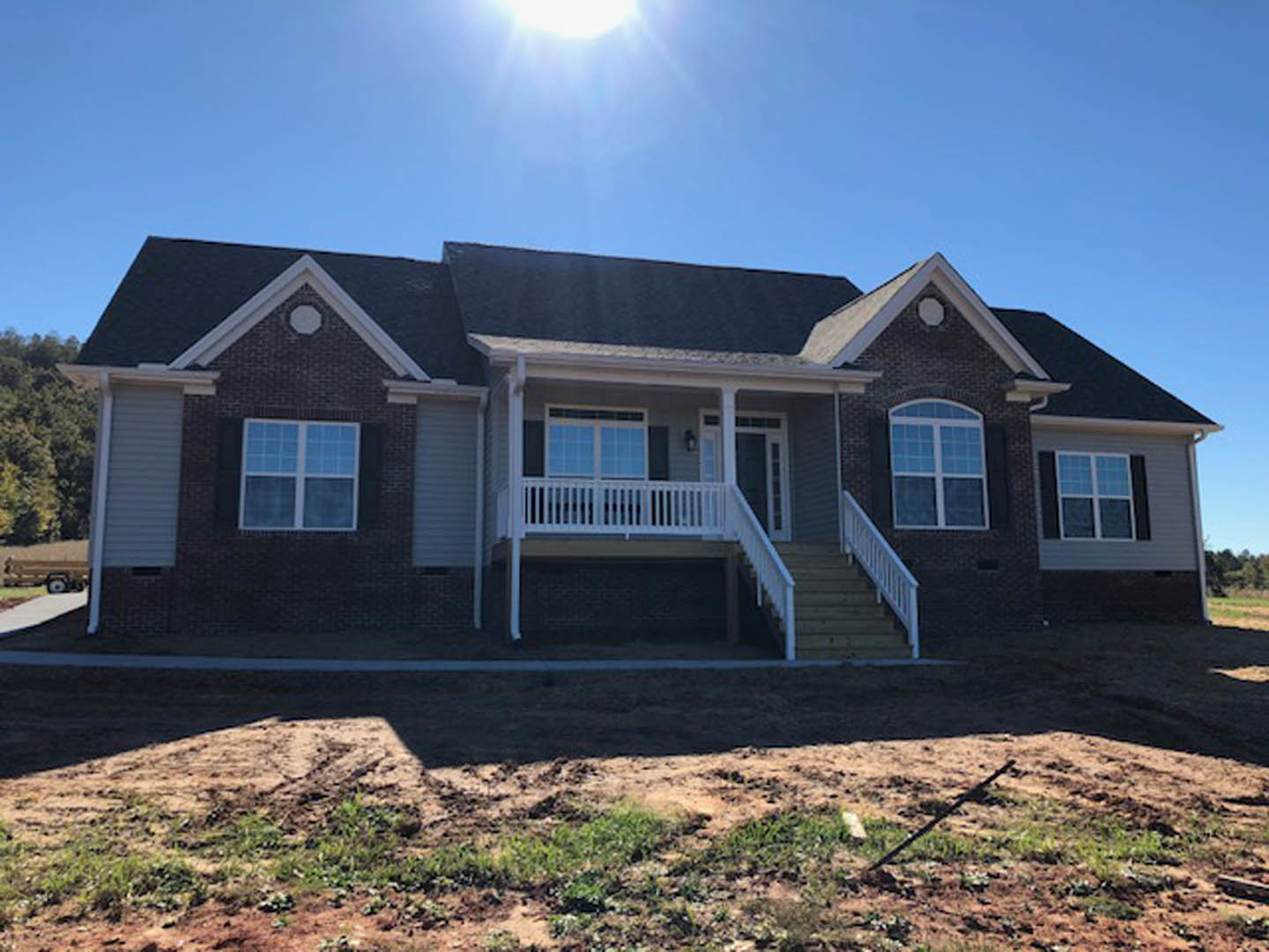 Two-story home with gray siding, covered front porch, white trim, multiple square windows, landscaped yard, and partly cloudy sky in background