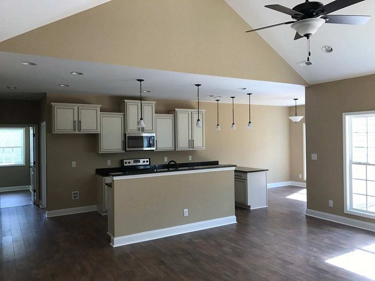 Open kitchen and dining area with wood cabinetry, granite countertops, stainless steel microwave, ceiling fan with light fixture, tile flooring, and window with white blinds.