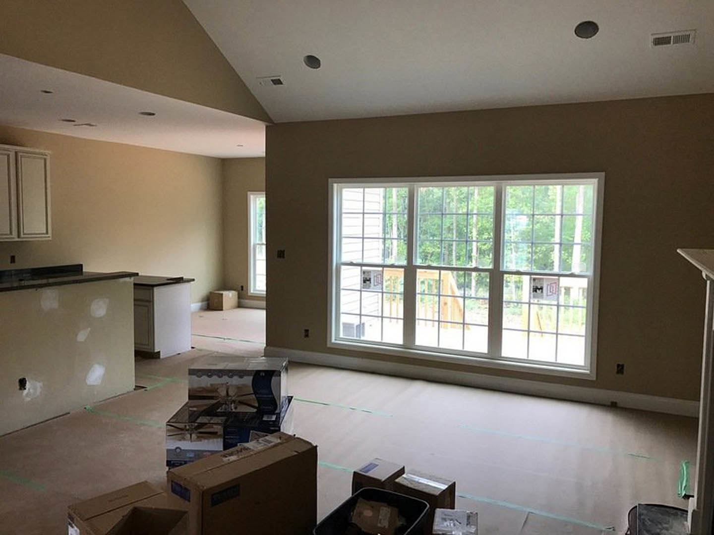 Spacious kitchen with large multi-pane window, white painted walls, light wood cabinetry, cardboard moving boxes on countertops and floor