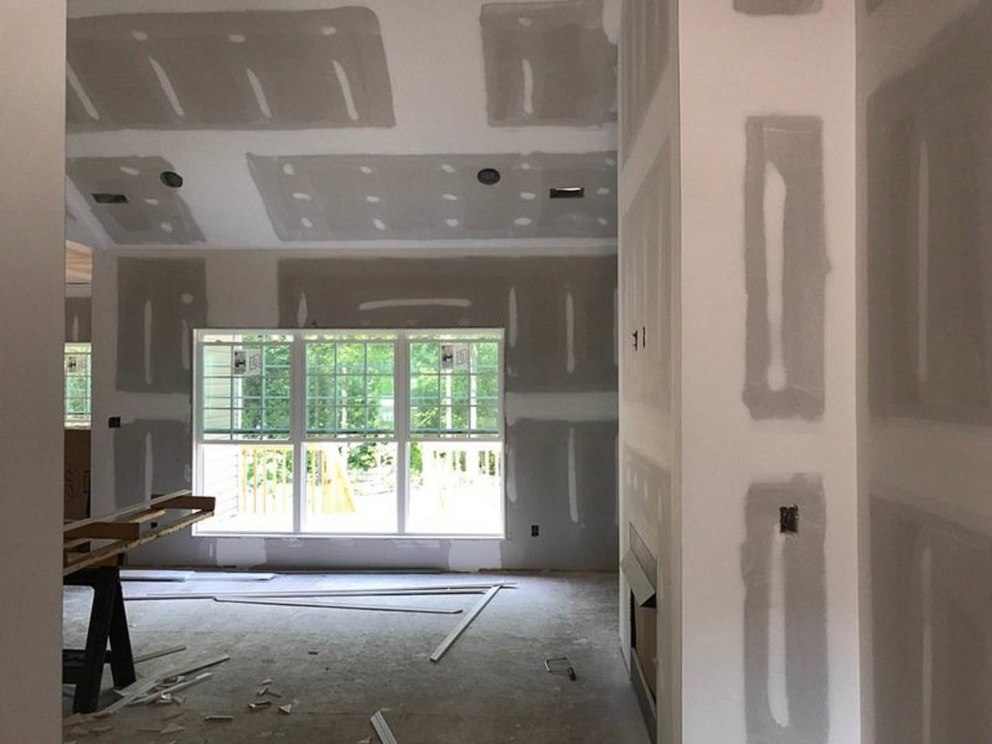 Sunlit room featuring a multi-pane window set in a grey plaster wall, with visible broken flooring and blurred hand in foreground.