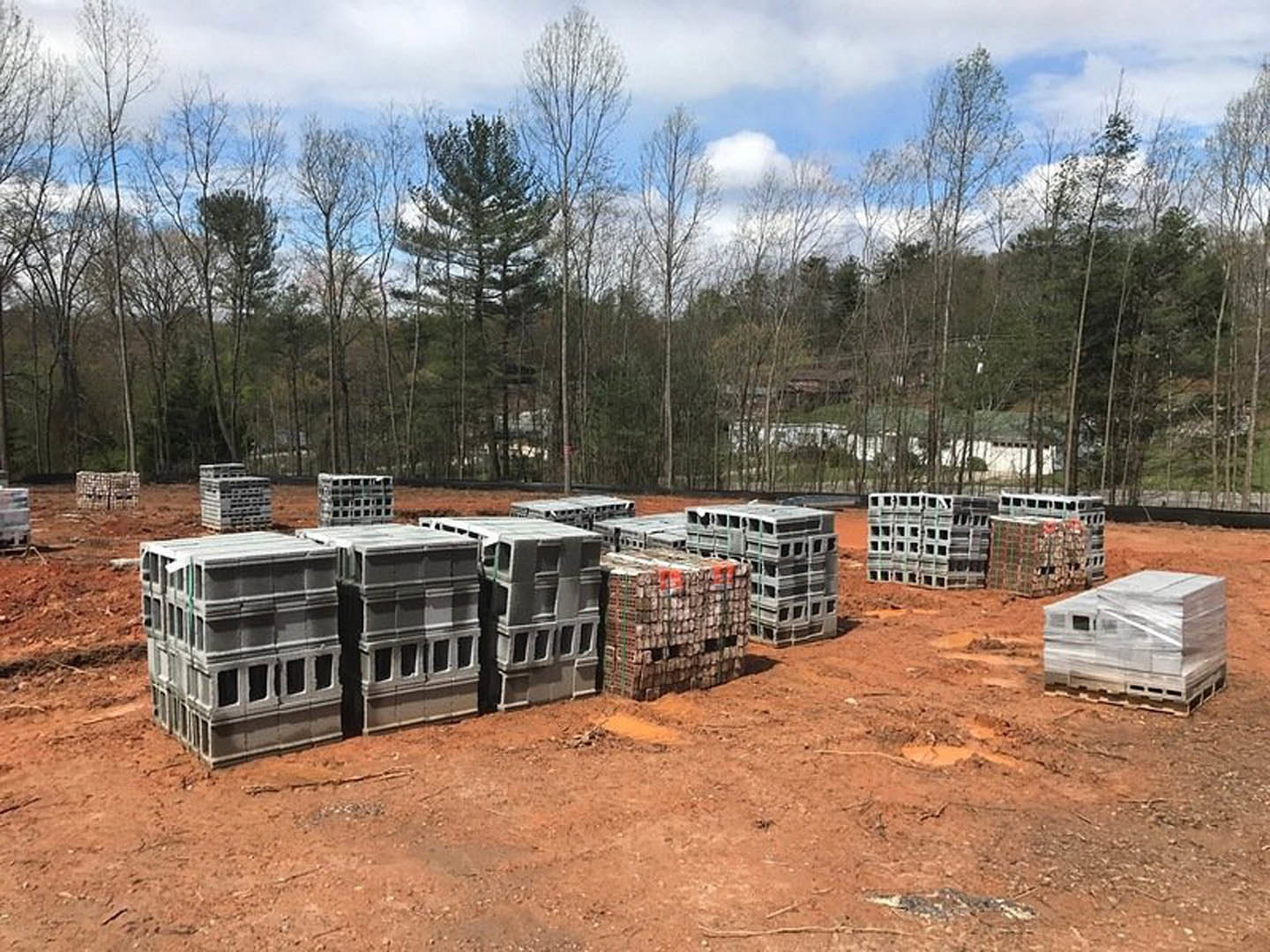 Stack of grey crates and pallets on a dirt field with scattered trees in the background under a cloudy sky