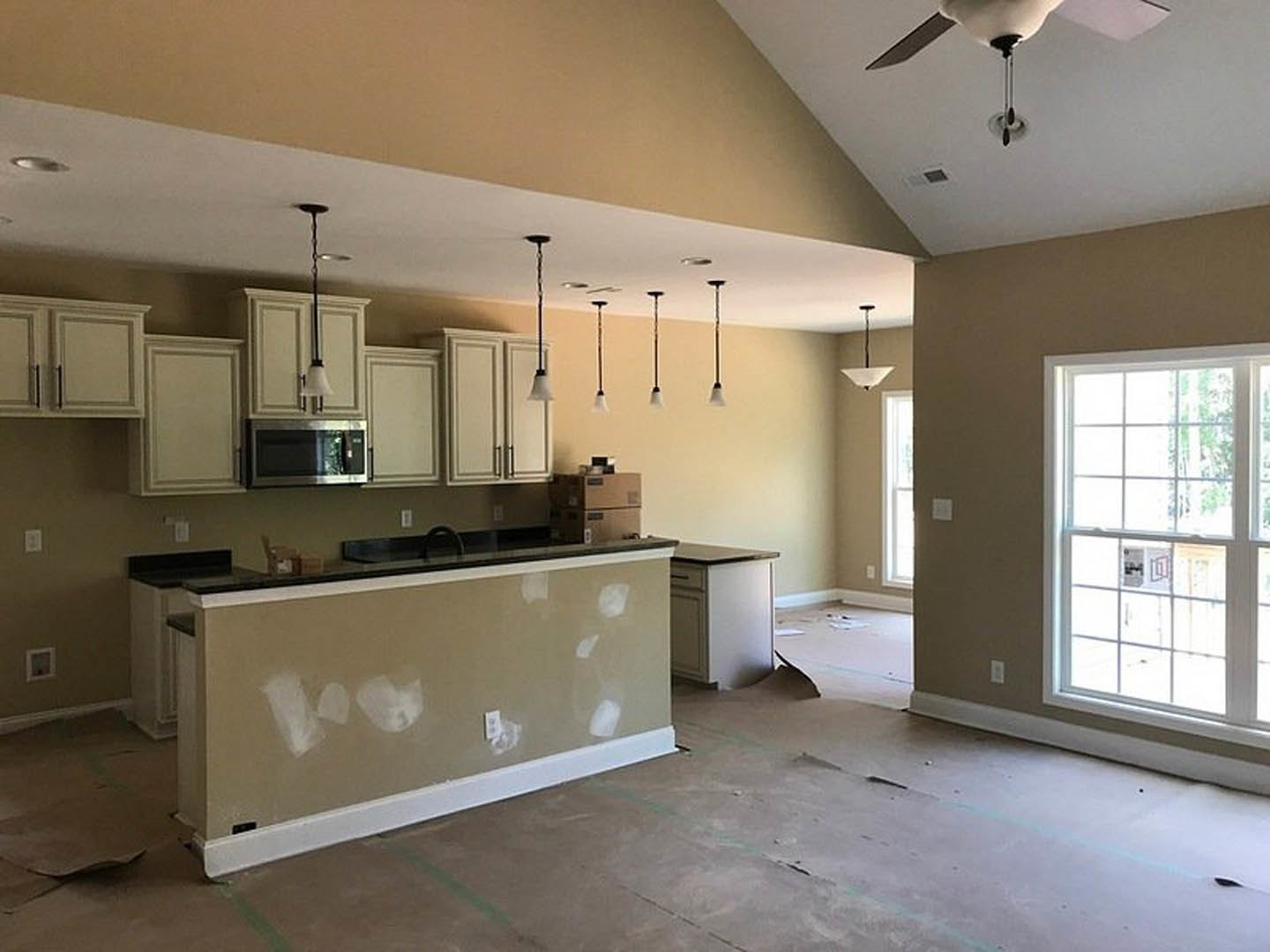 Open kitchen with white cabinetry, stone countertop bar, stainless steel sink, multi-pane window, ceiling fan, and white painted walls