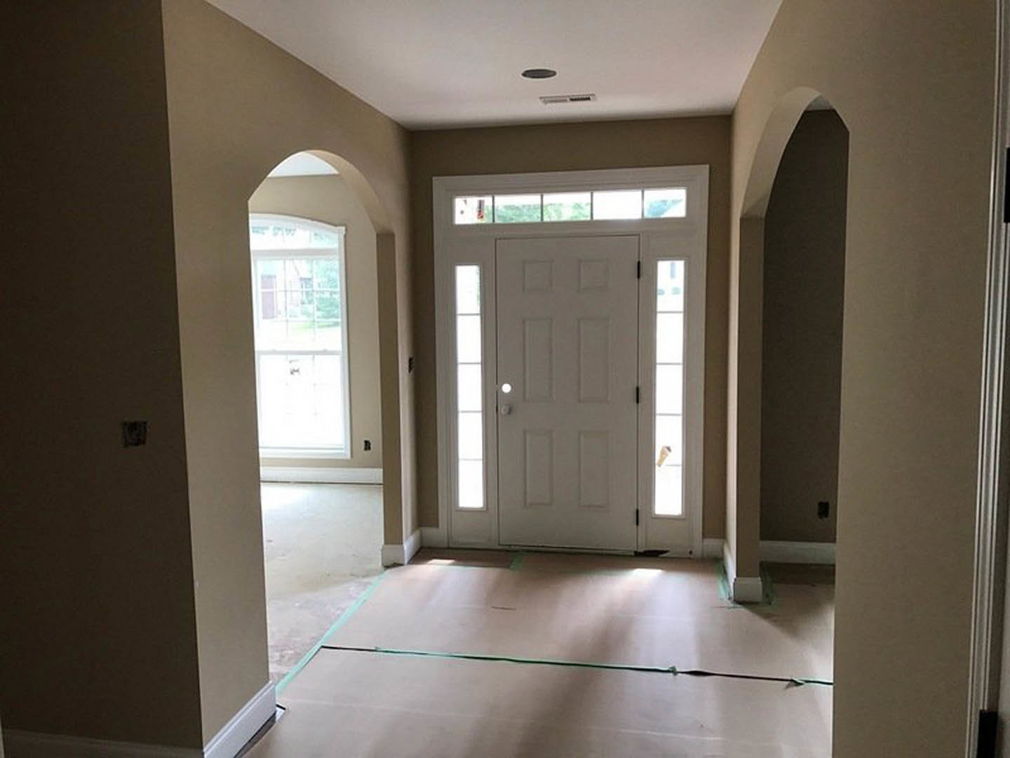 Hallway with arched doorways, white paneled door featuring glass windows, light switch on plaster wall, hardwood flooring, window offering outdoor view