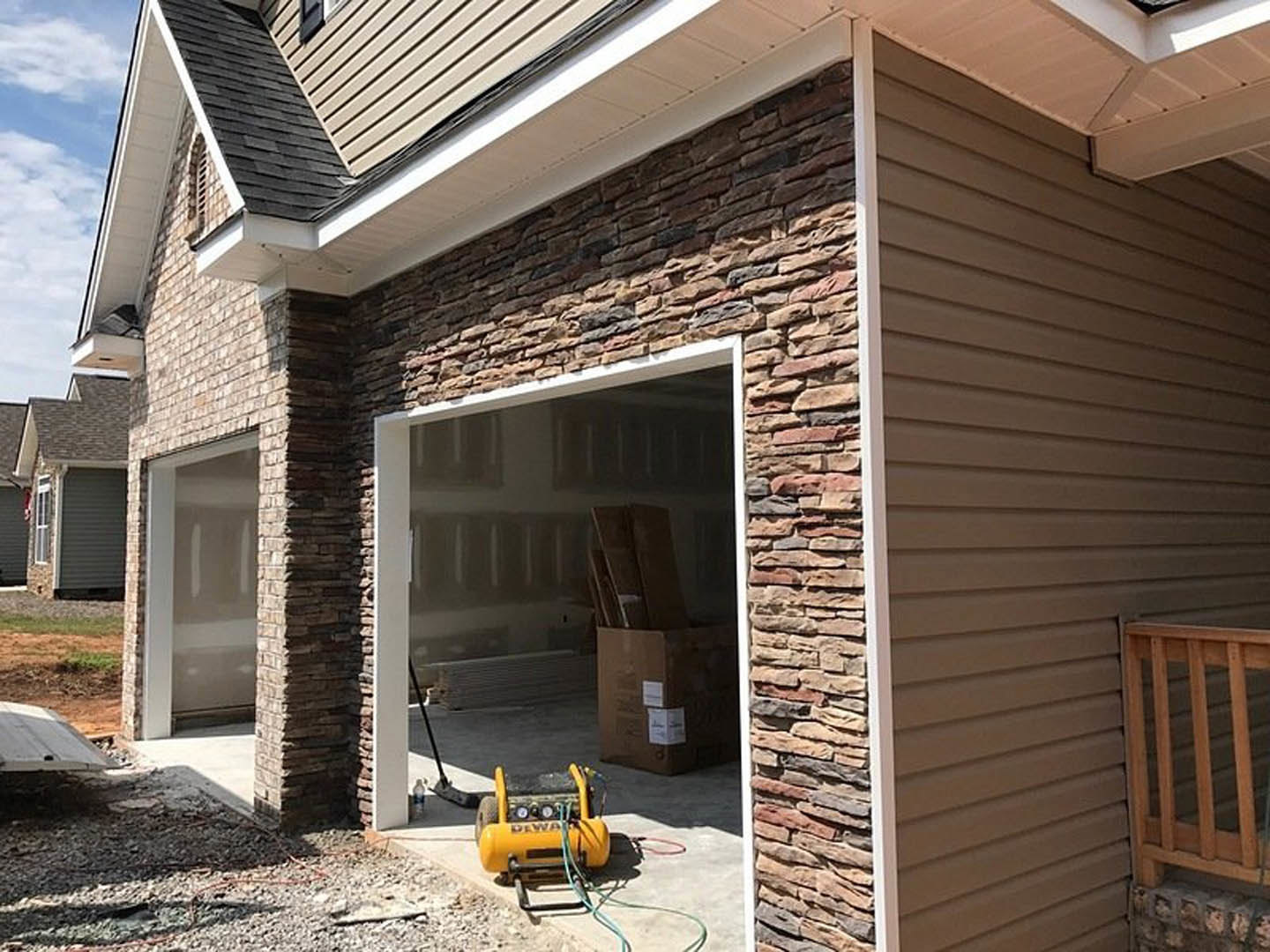 Modern home exterior with white siding, large garage door, wooden railing along entry steps, multiple windows, concrete driveway, and landscaped front yard.