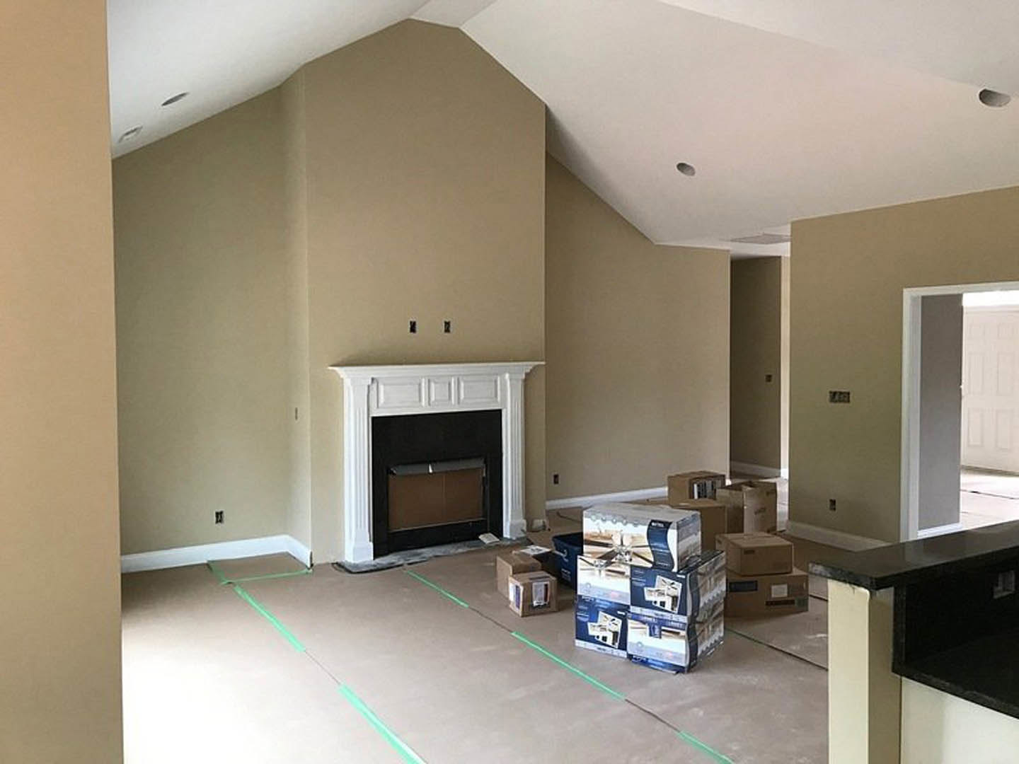 Living room with white-trimmed fireplace, black countertop, stacked moving boxes on a table, green tape marking hardwood floor, and dark cabinetry.