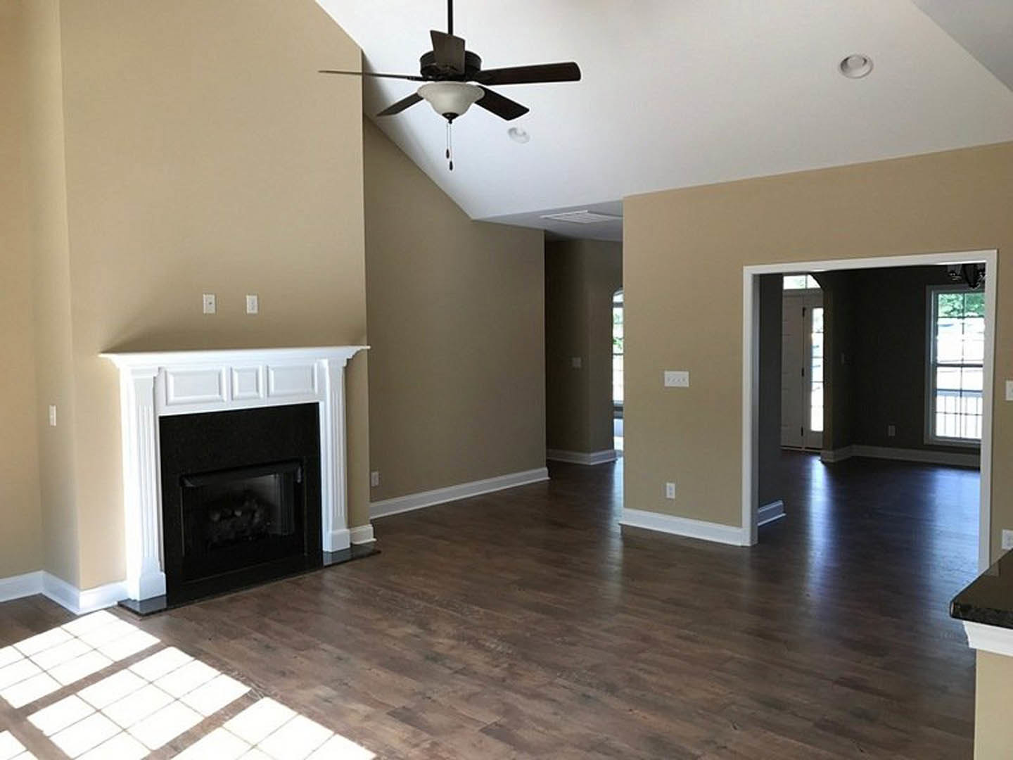 Living room with wood flooring, white-trimmed fireplace, ceiling fan with light fixture, and white tile hearth