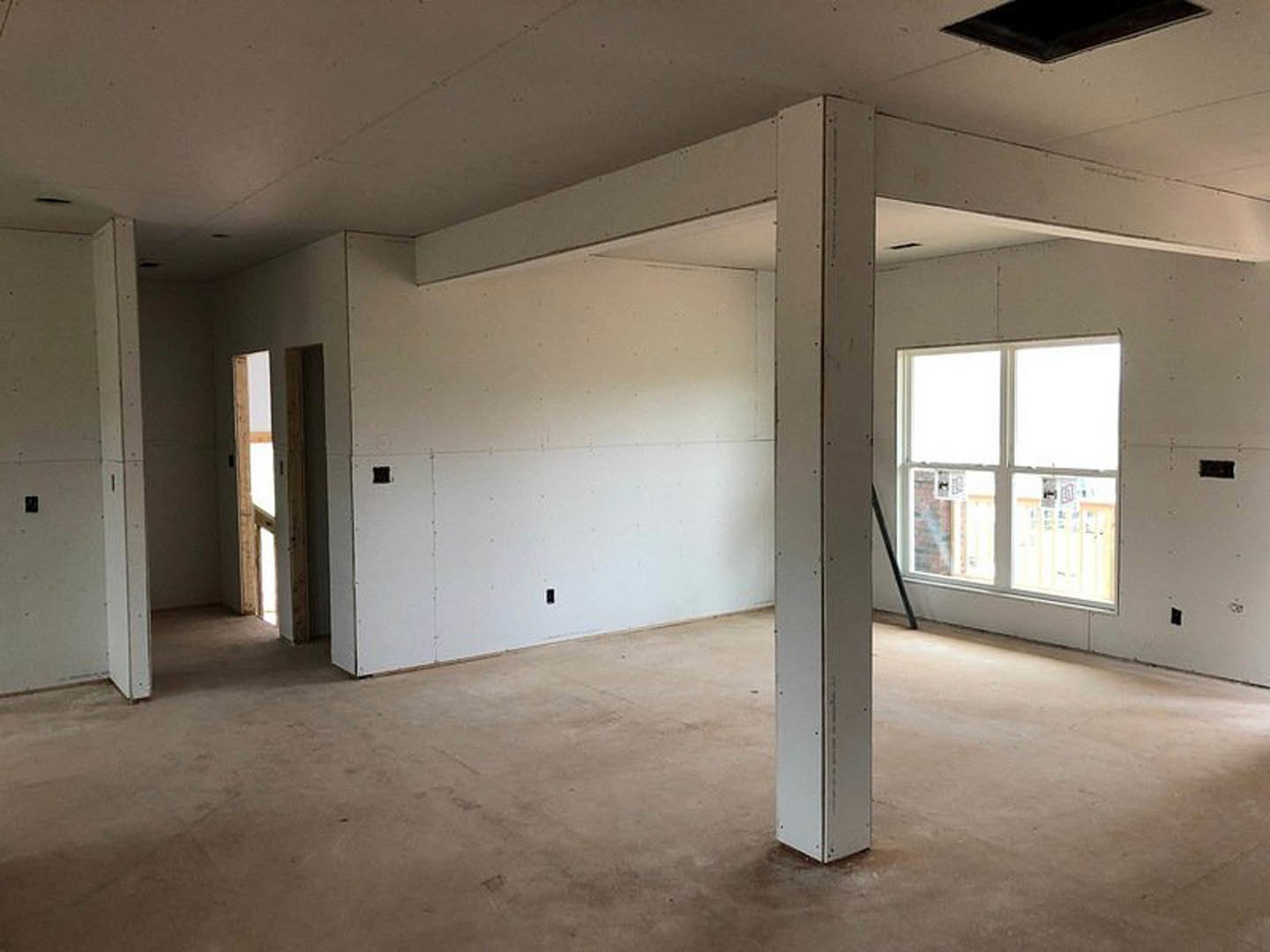 Open living space with concrete flooring, white walls, central structural pillar, large window with white frame, and modern black door handle