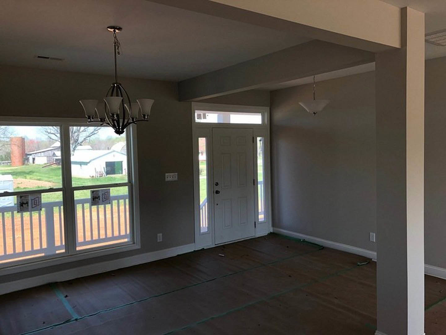 Dark wood flooring, white walls, white door with black handle, large windows, modern chandelier hanging from ceiling