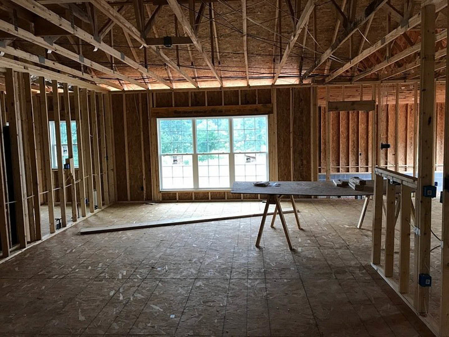 Dining area with exposed wood ceiling beams, multi-pane window, wooden table, and black wall-mounted box