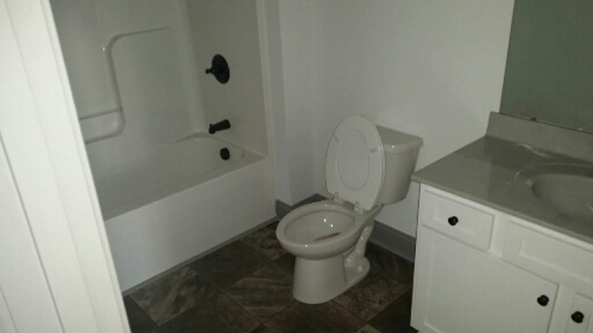 White porcelain toilet with seat up, set against light tile wall in bathroom with visible plumbing fixtures and partial sink.