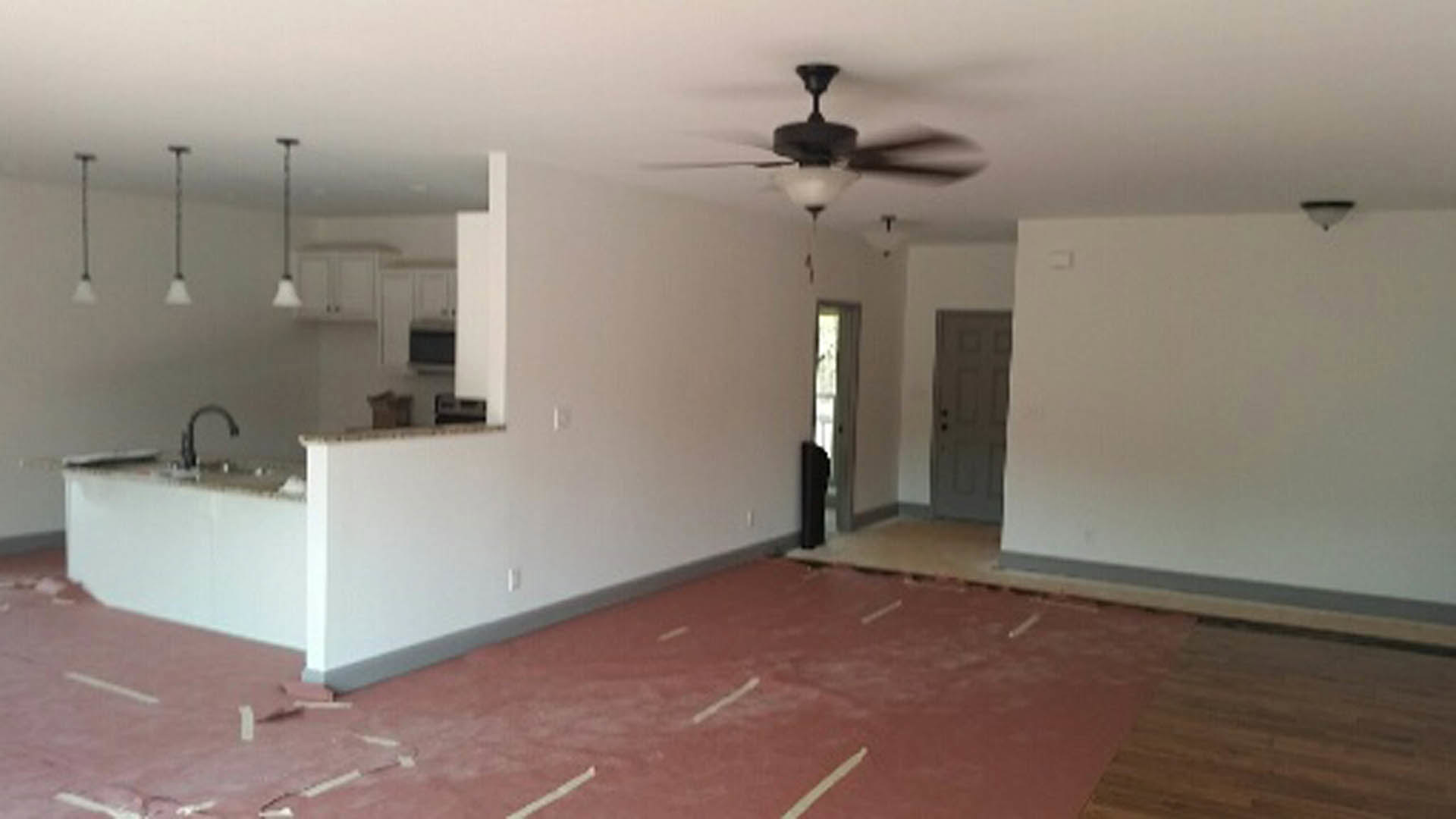 Ceiling fan with light fixture above red flooring, plaster walls, and window in residential room