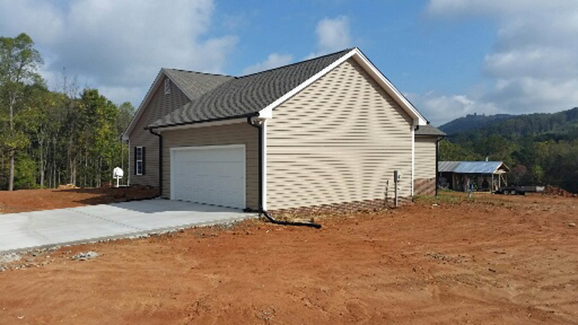 White two-story house with attached single-car garage, white paneled garage door, light gray siding, black hose coiled near the entrance, concrete driveway, mature trees in