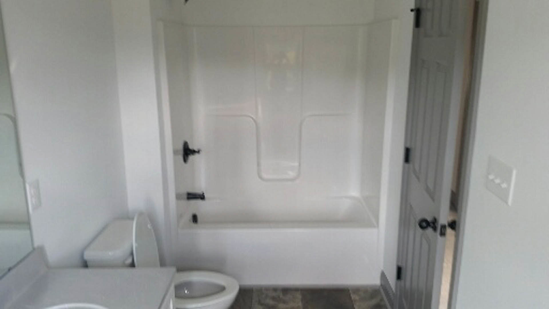 White porcelain toilet with lid open next to a built-in bathtub, surrounded by light-colored tile walls and floor.