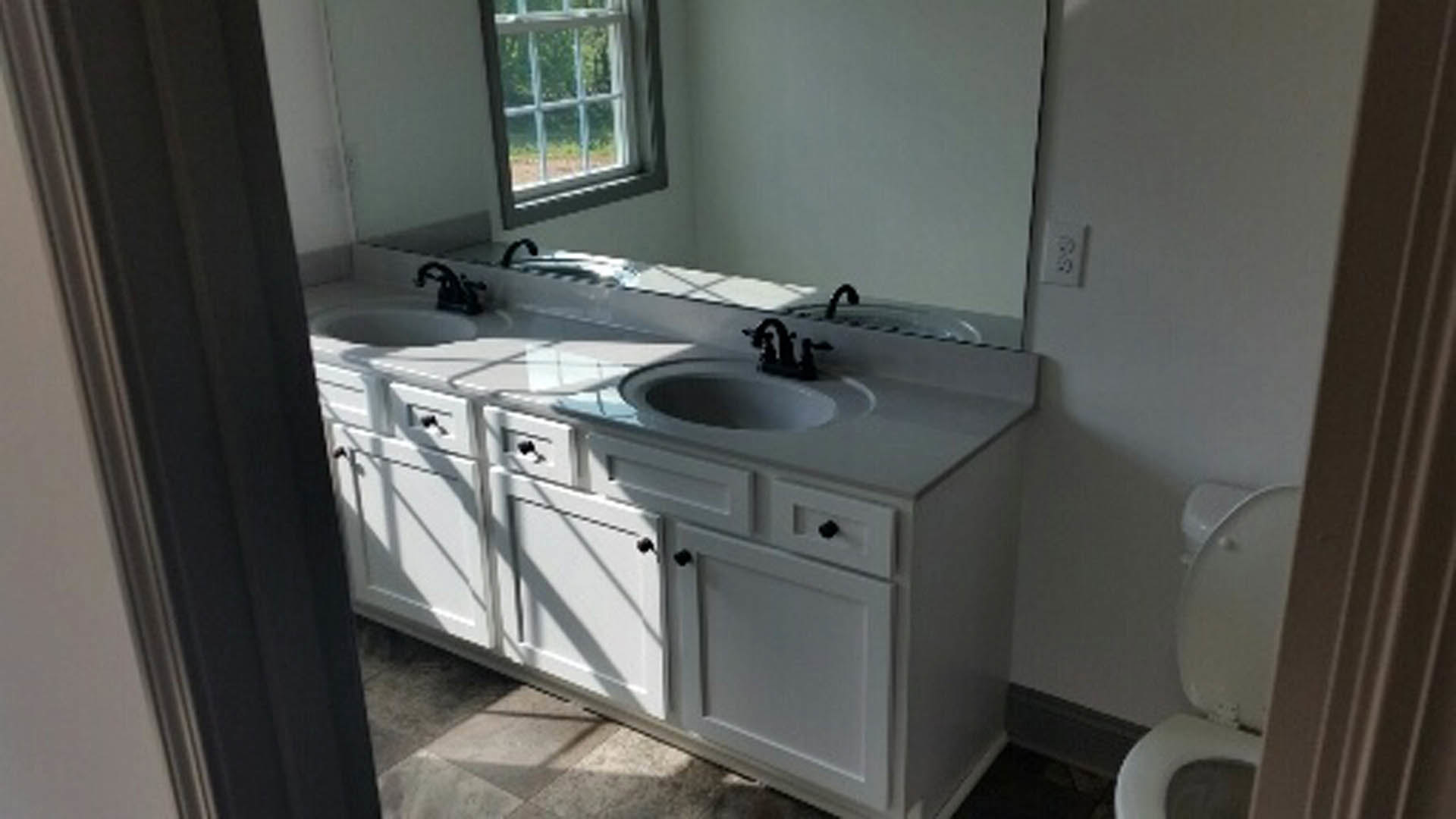 Bathroom with double vanity, wide mirror above sinks, open toilet lid, light tile flooring, white cabinetry, chrome faucets, neutral wall color