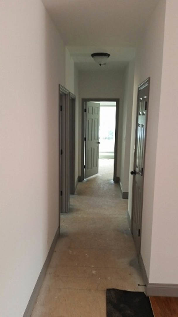 Hallway with laminate flooring, white plaster walls, two white doors, one door illuminated by bright light, black door handle, wood surface detail