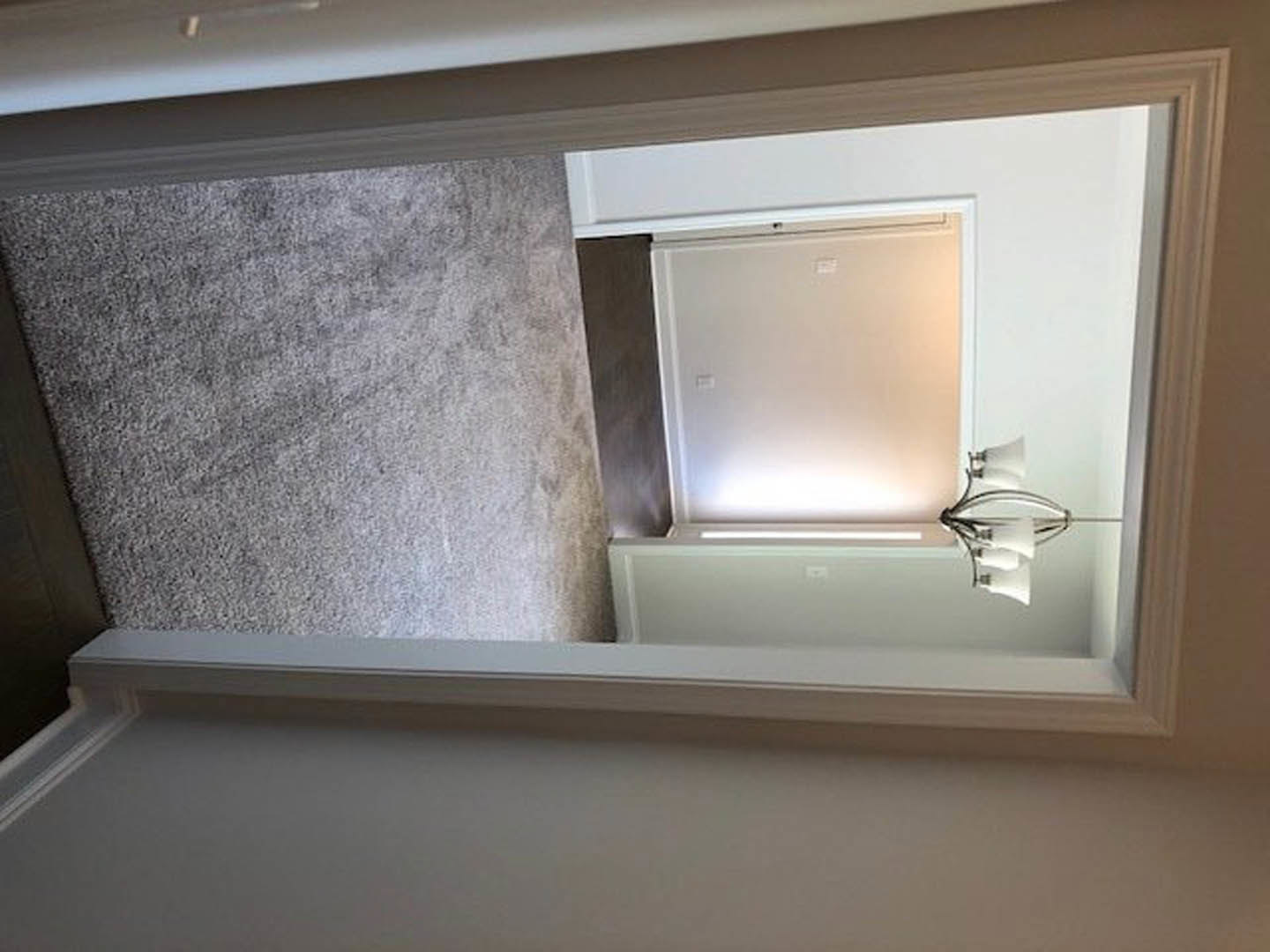 Hallway with white walls and trim, white door featuring a black handle, carpeted floor, and a close-up view of a chandelier-style light fixture.