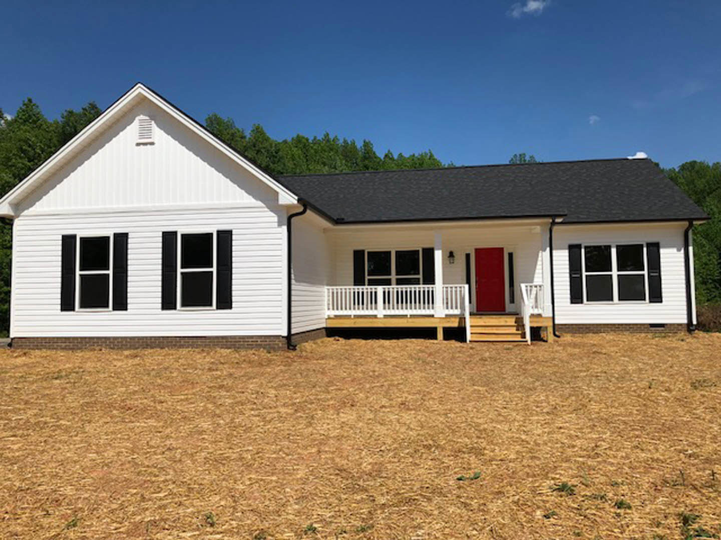 White siding house with red front door, white-framed windows, covered porch, and white picket fence under partly cloudy sky.