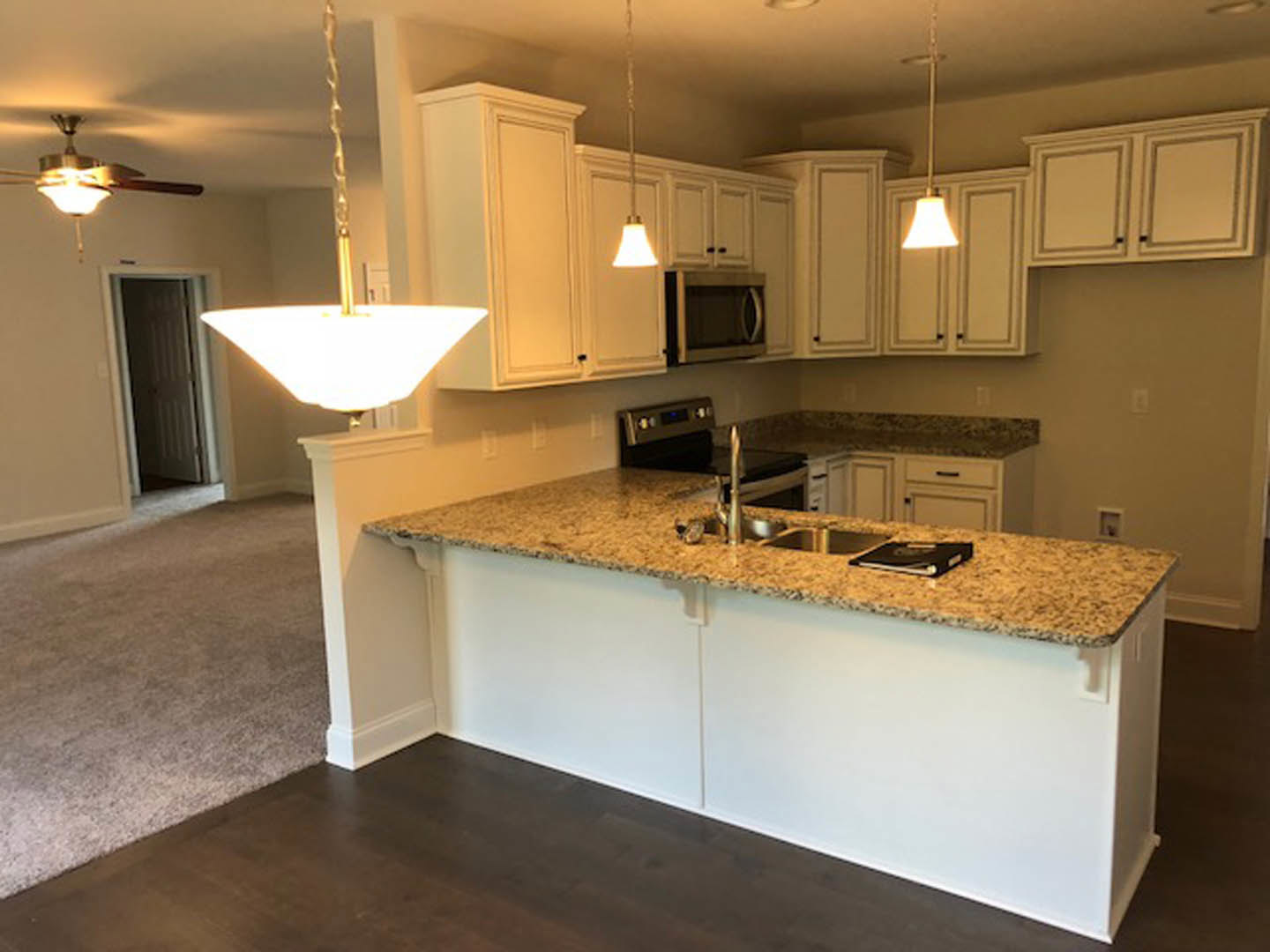 Marble countertop kitchen with white ceiling, open microwave door, white-shaded bell light fixture, cabinetry, sink, and appliances