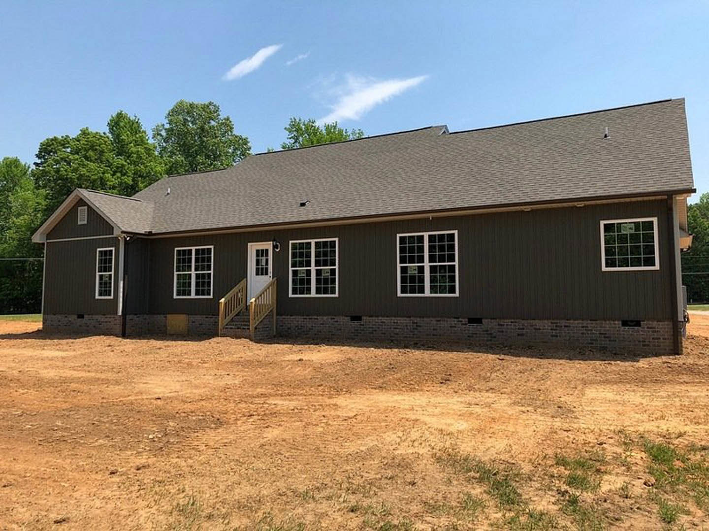 Two-story house with white-framed windows, brick exterior, and a dirt yard in front; staircase visible through a window, sign posted on one window.