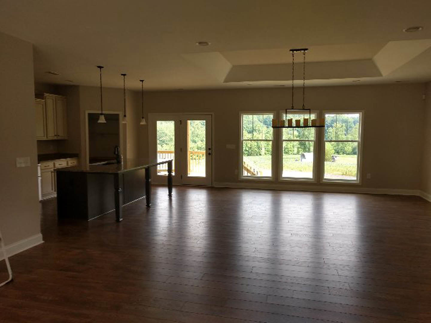 Spacious open floor plan featuring a central kitchen island, dark dining table, wood flooring with natural light reflections, double glass-paneled doors, large windows, and a door