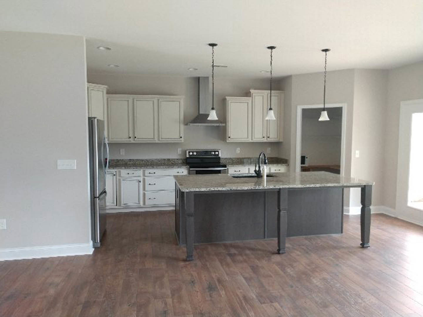 Kitchen with marble island countertop, black oven, stainless steel refrigerator, white three-door cabinets, wood flooring, and metal pole.