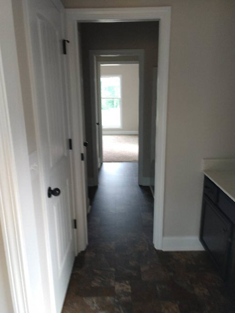 Hallway featuring smooth white walls, dark wood plank flooring, white doors with silver handles, and recessed ceiling lighting